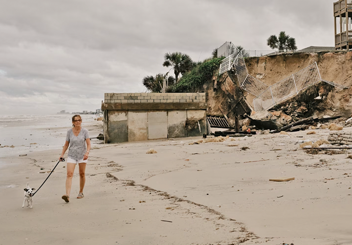 A woman walks her dog on a Florida beach near a portion of hillside destroyed by a hurricane. 